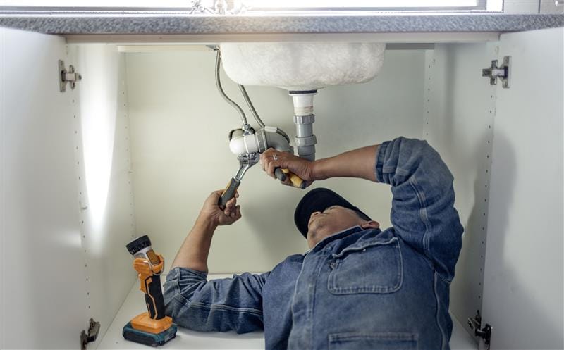 Plumber repairing pipes beneath a bathroom sink in Miami