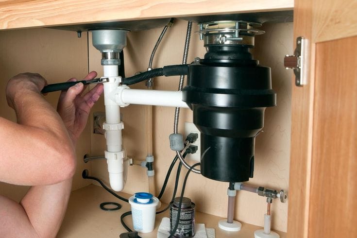 Plumber installing a garbage disposal beneath a kitchen sink in Miami