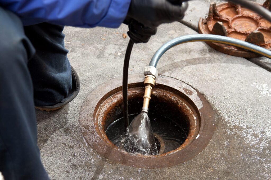 Plumber hydro jetting a sewer line through a manhole in Miami