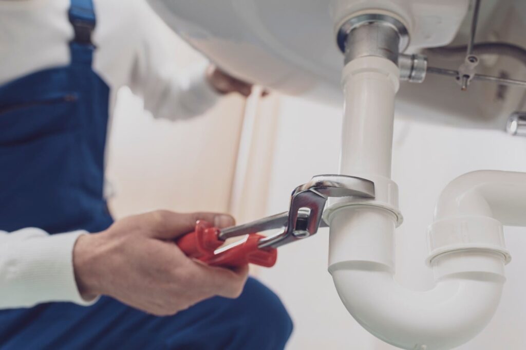 Plumber repairing a white drain pipe beneath a sink in Miami