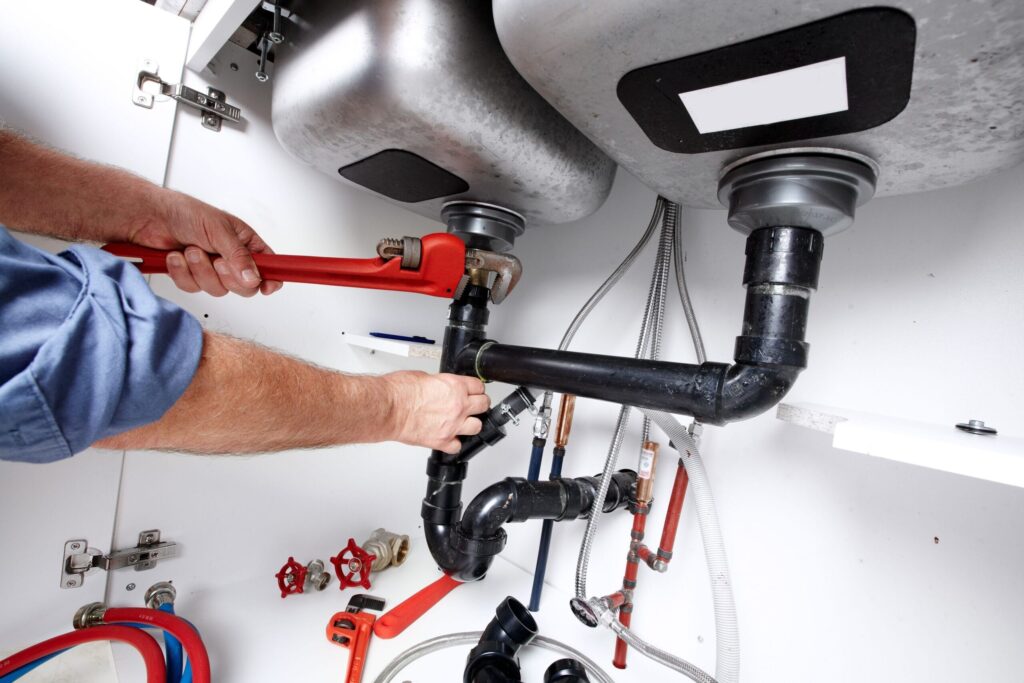 Plumber repairing drain pipes beneath a kitchen sink in Miami